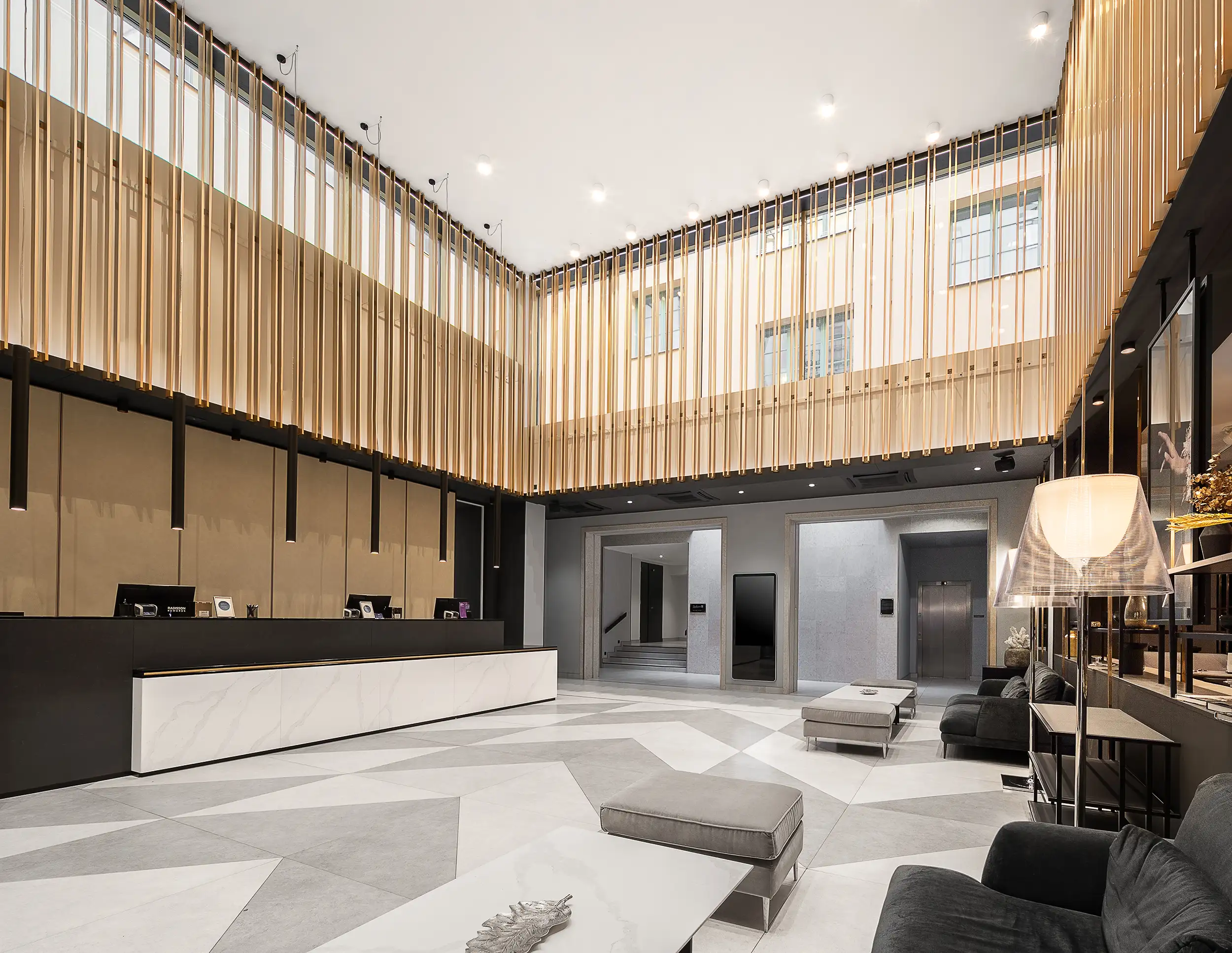 großzügige hotel lobby mit hoher decke, vertikalen goldfarbenen lamellen, moderner rezeption und lounge bereich