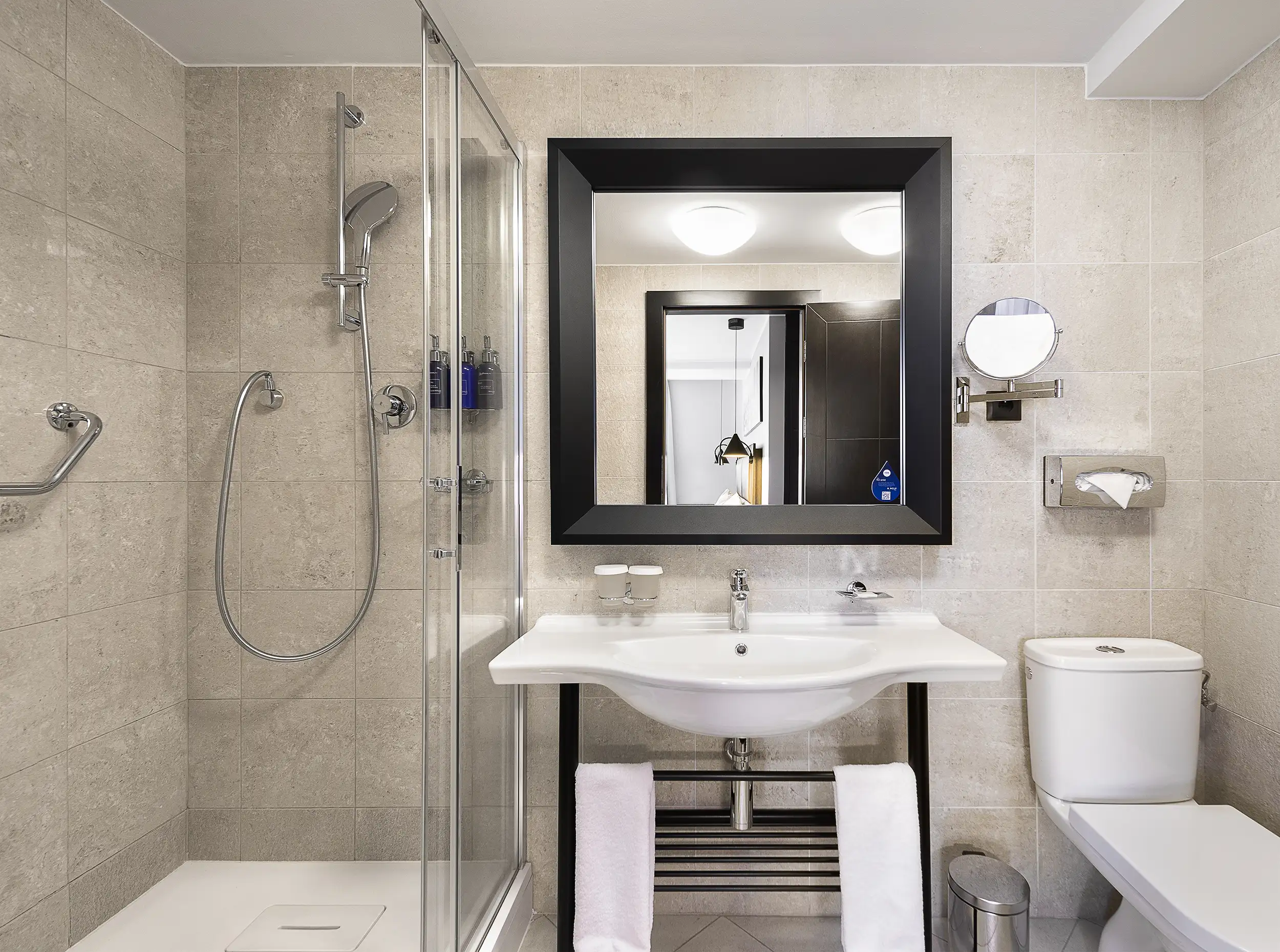 Modernes Badezimmer im Radisson Blu Prague mit verglaster Dusche, großem Wandspiegel und hellem Natursteinfliesen