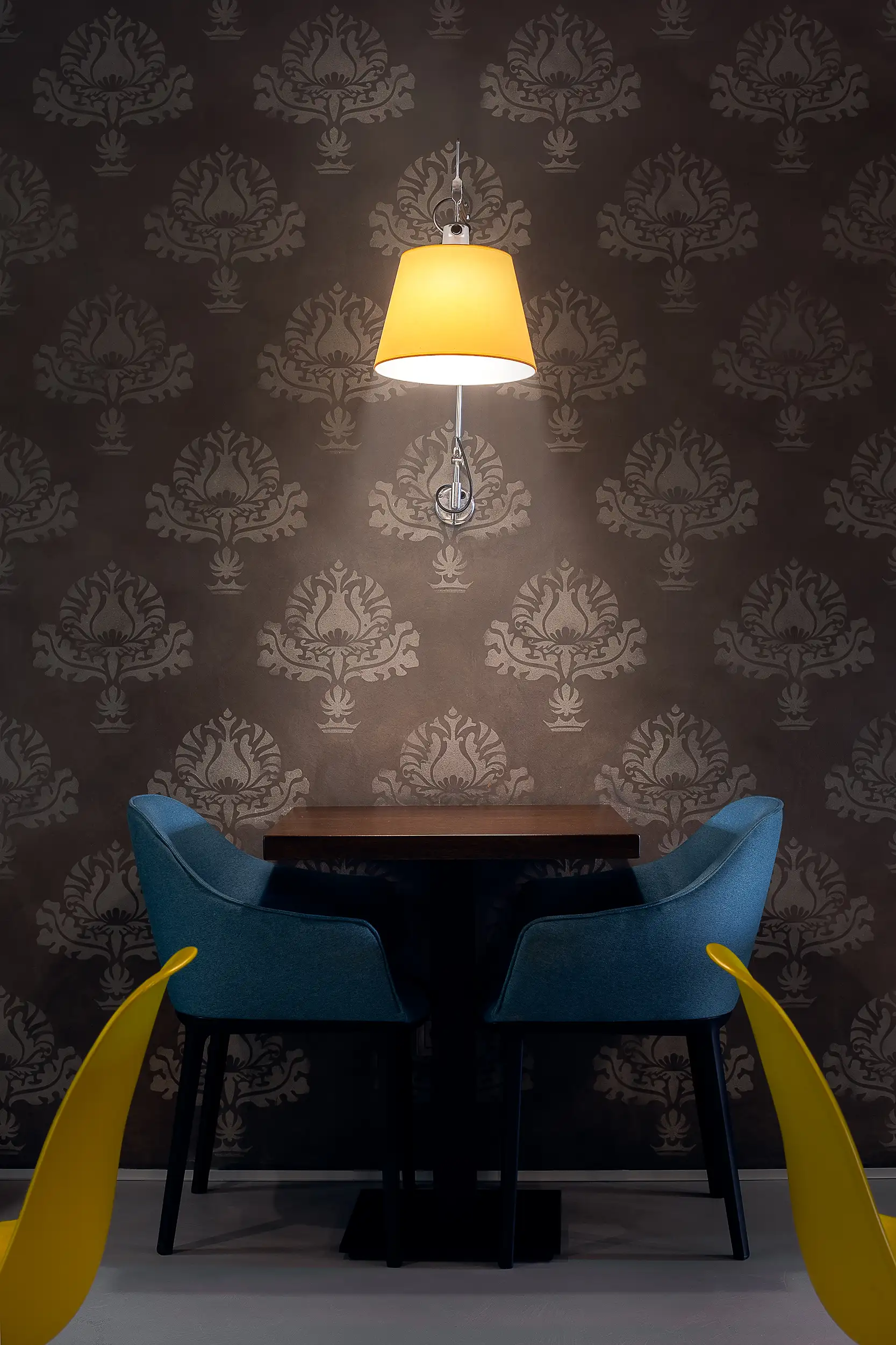 Symmetrischer Detailblick auf Sitznische im Frühstücksraum mit gepolsterten Sesseln, dunkler Mustertapete und warmer Wandbeleuchtung.