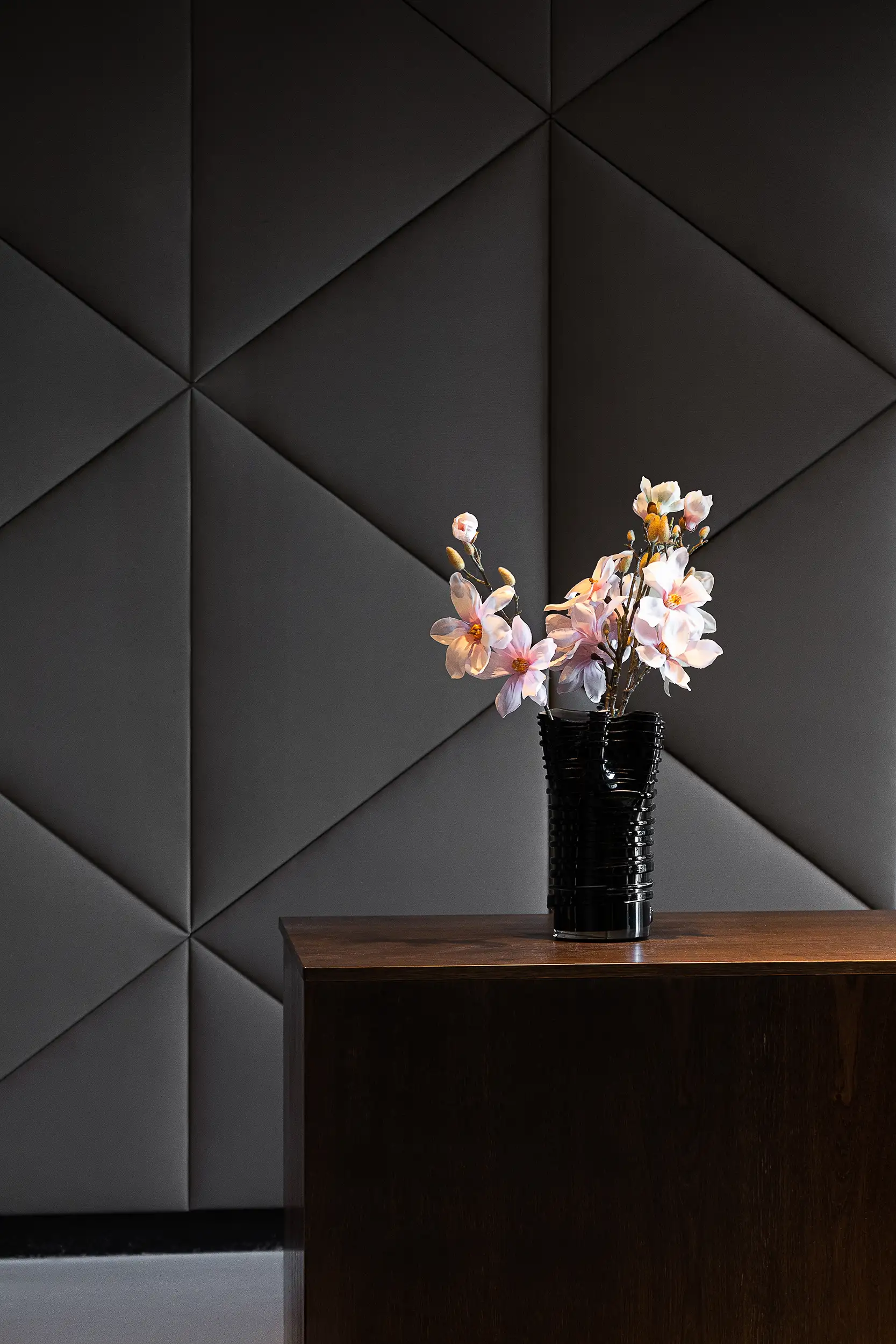 Detailaufnahme aus der Lobby des MOODs Boutique Hotel Prag mit Blume auf dem Empfangstresen vor polygonaler Wandgestaltung.