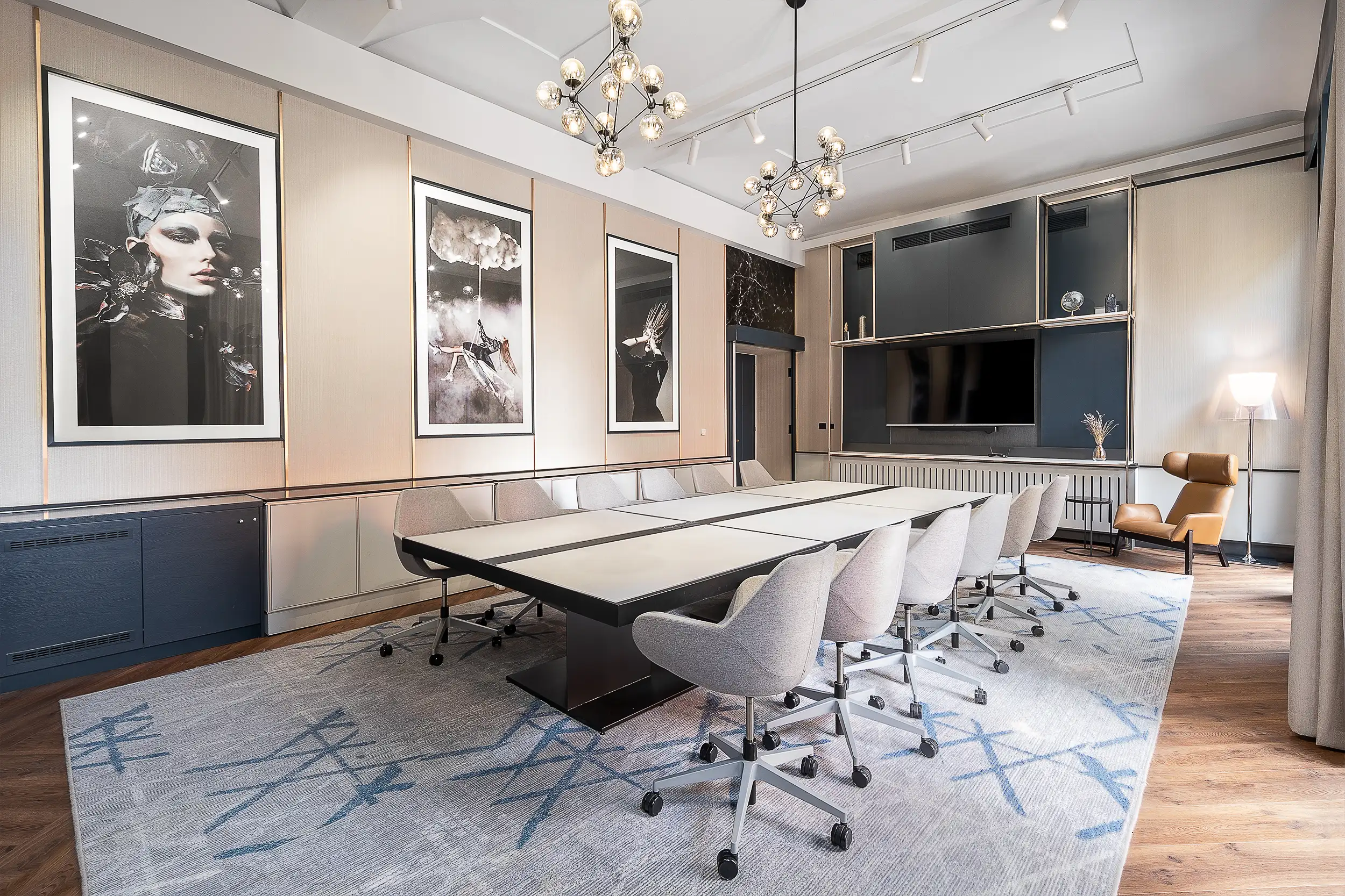 Hotelová zasedací místnost Stylish v Radisson Blu Praha s velkým stolem a šesti židlemi po obou stranách, uměleckými díly na stěnách a pohodlným křeslem a lampou v rohu místnosti.