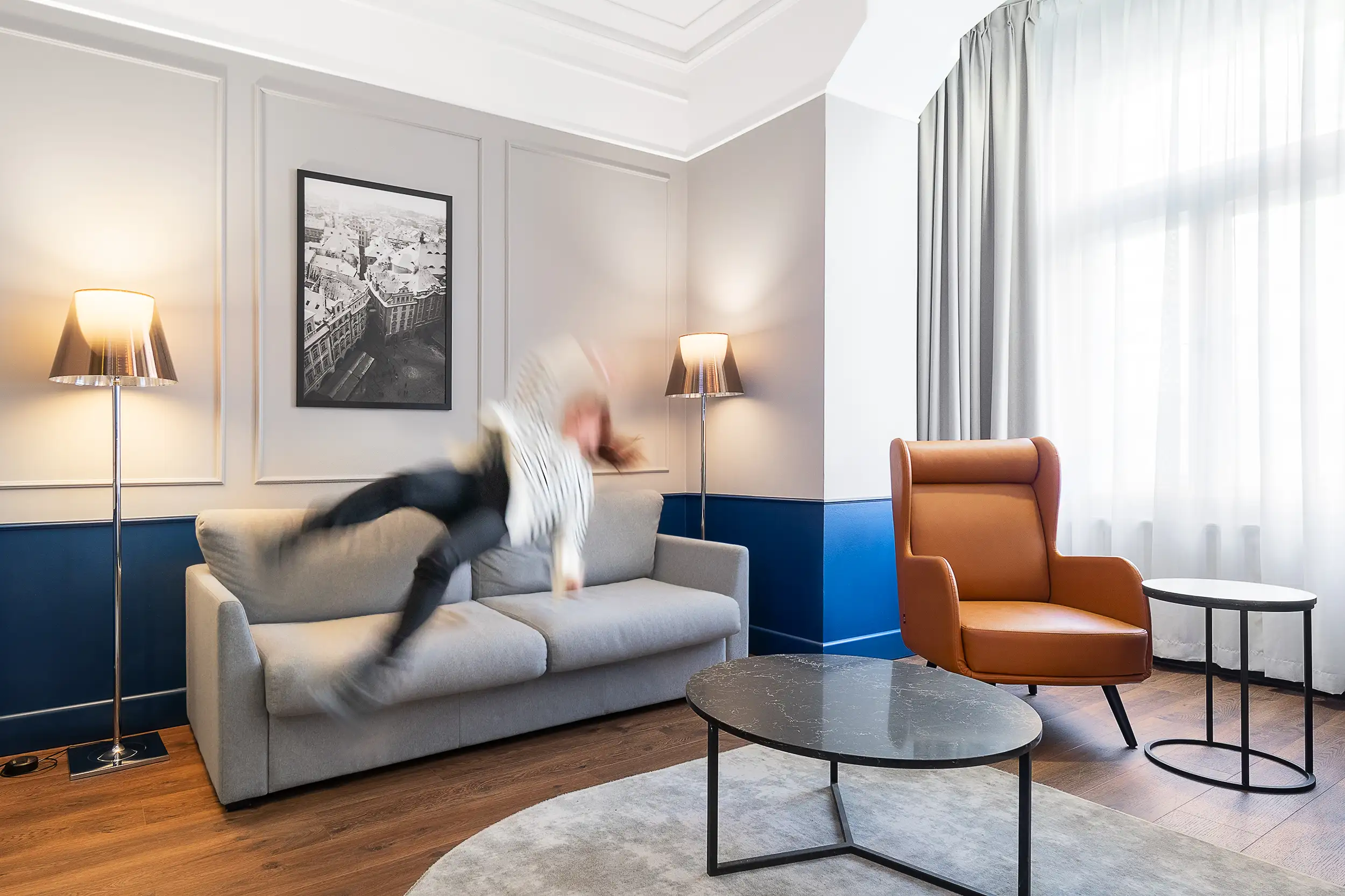 Konzeptionelles Hospitality-Foto einer fliegenden Frau, die in Bewegung verschwommen ist und scheinbar auf einem Sofa in der Junior Suite des Radisson Blu Hotels in Prag springt.