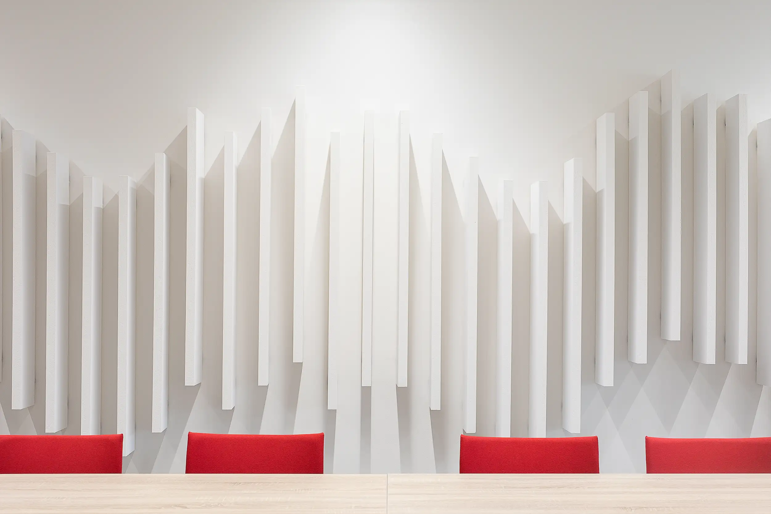 Detail of the white wall-mounted acoustic design panels in the Doosan Bobcat conference room positioned to wave shape combined with red chairs in Dobris, Czech Republic.