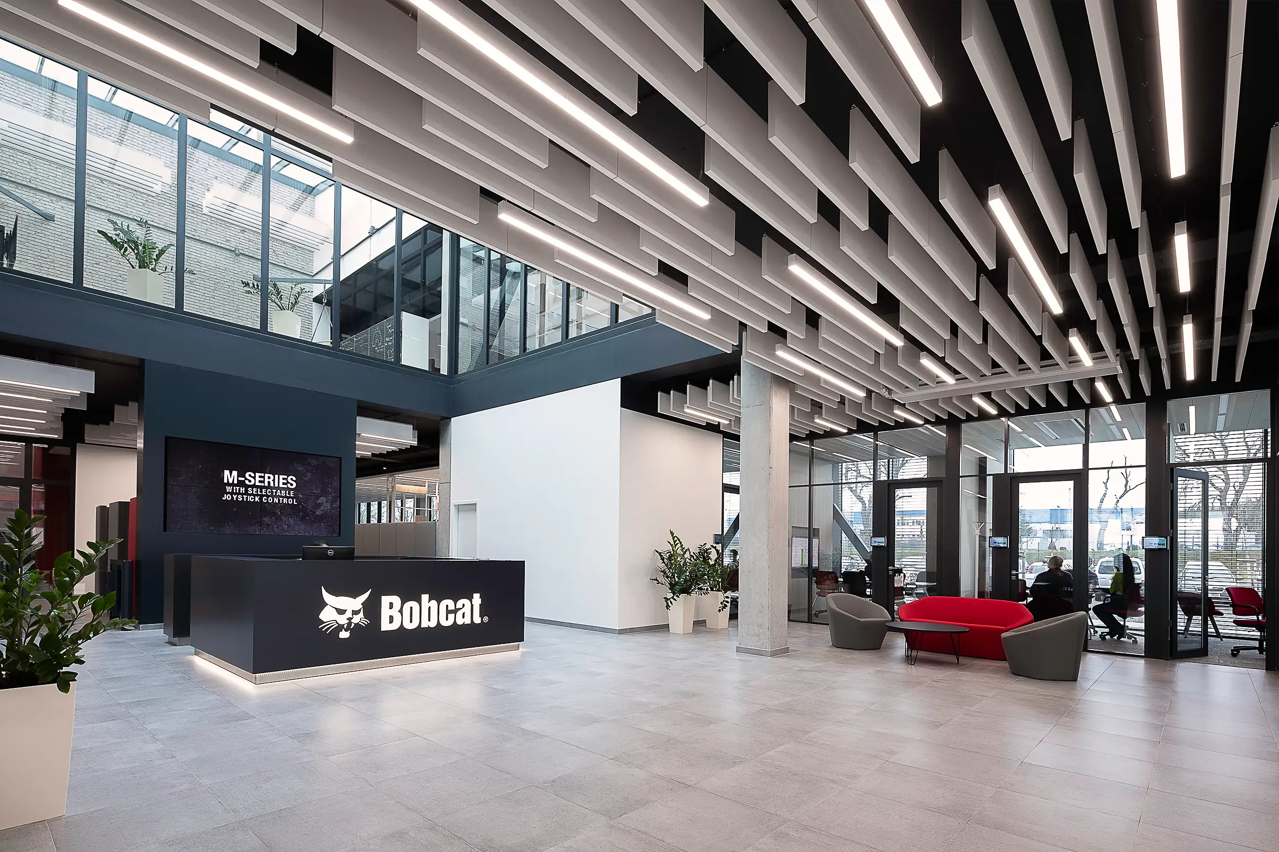 Interior photography of the lobby and reception area of Doosan Bobcat in Dobris, Czech Republic, focusing on the acoustic ceiling panels with a glazed second floor.
