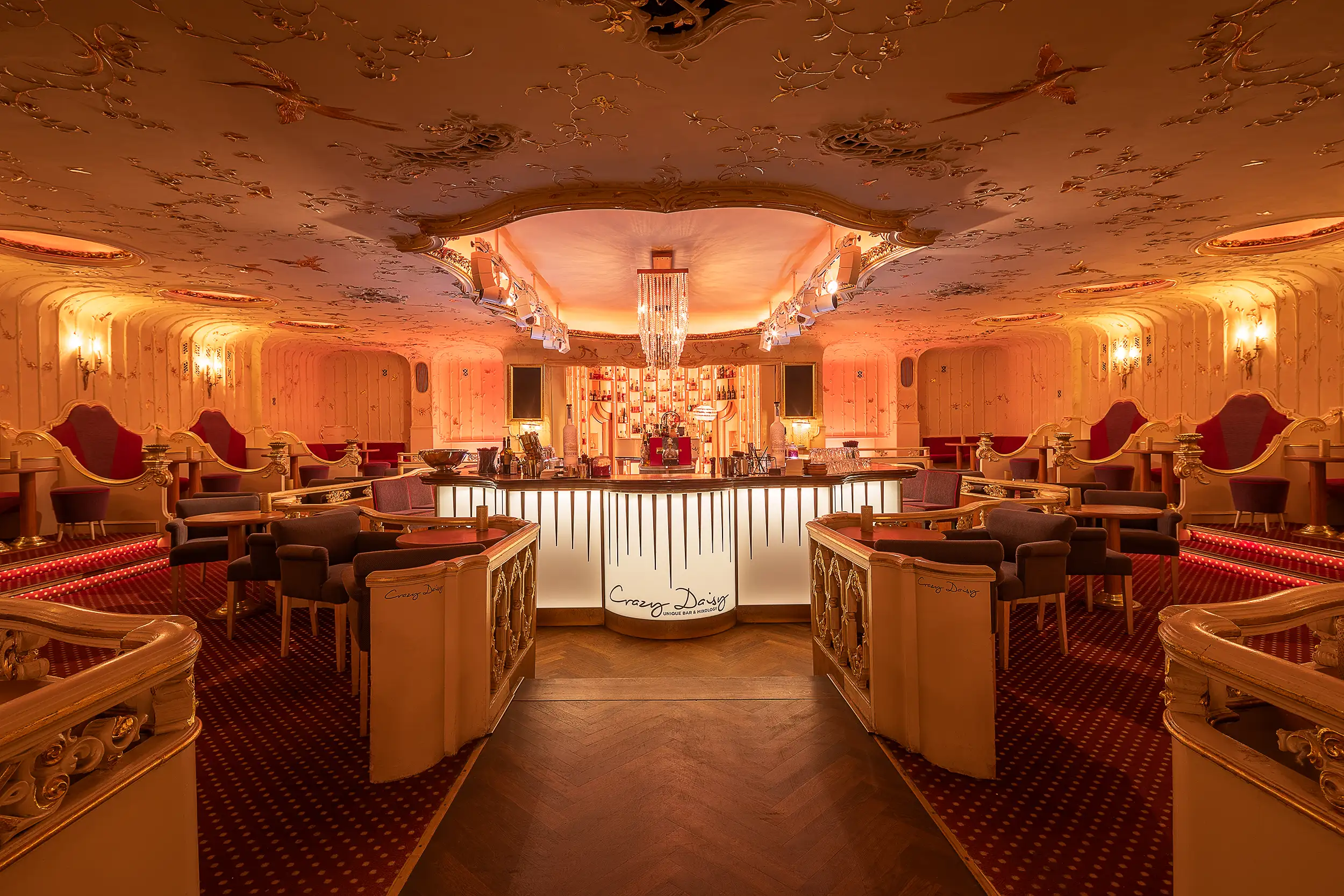 Photograph of a symmetrical space, interior of an Art Nouveau cocktail bar - Crazy Daisy in Prague, Czech Republic, decorated in red-orange colors.