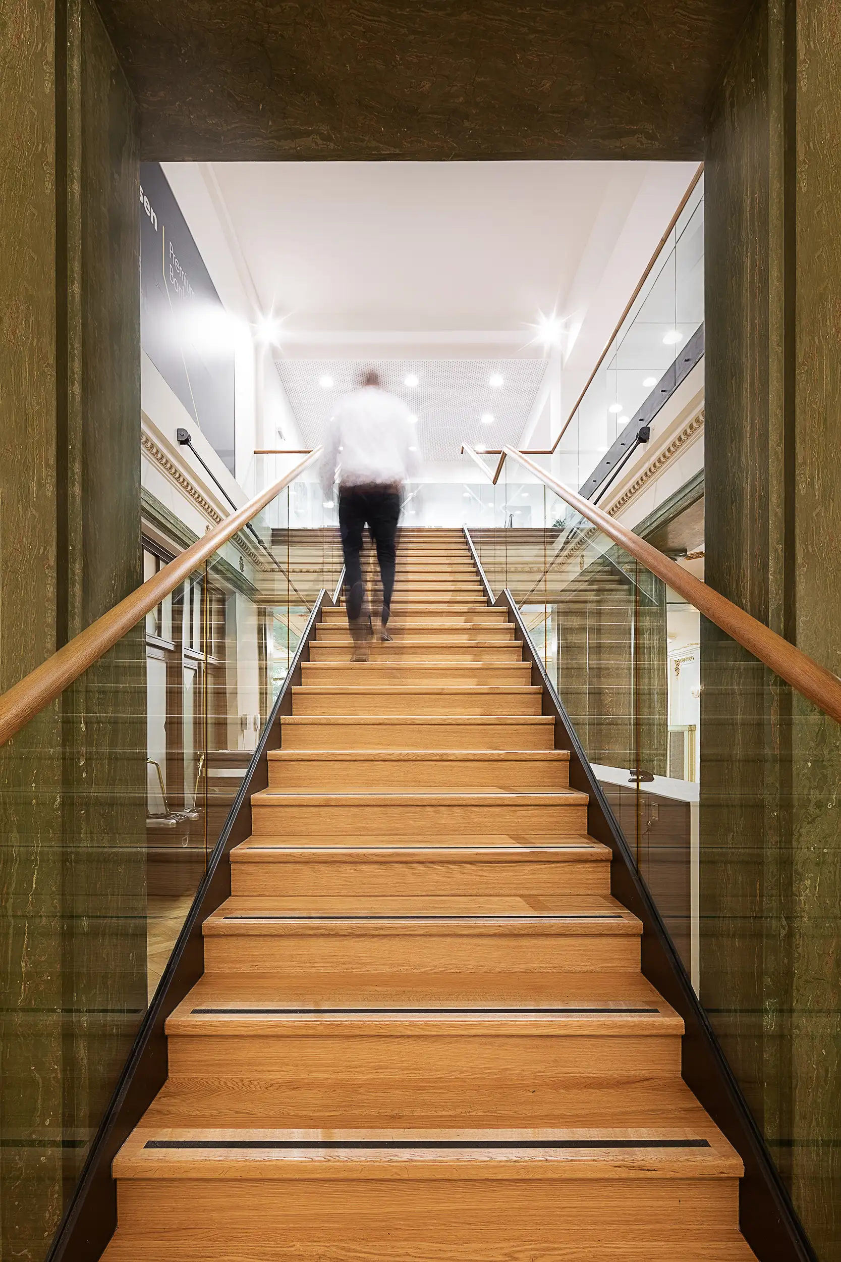 A man blurred by motion is climbing the stairs in a green-cream toned interior of Raiffeisenbank at Palace Astra on Wenceslas Square in Prague, Czech Republic.