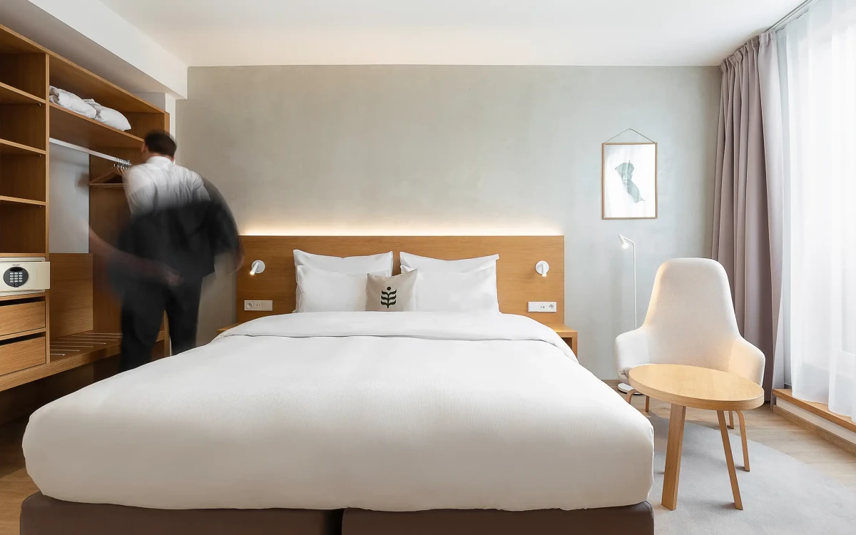 Botanique Premium King mit Balkon im Botanique Hotel Prag mit Kingsize-Bett und offenem Stauraum, Geschäftsmann in Bewegung unscharf im Hintergrund.