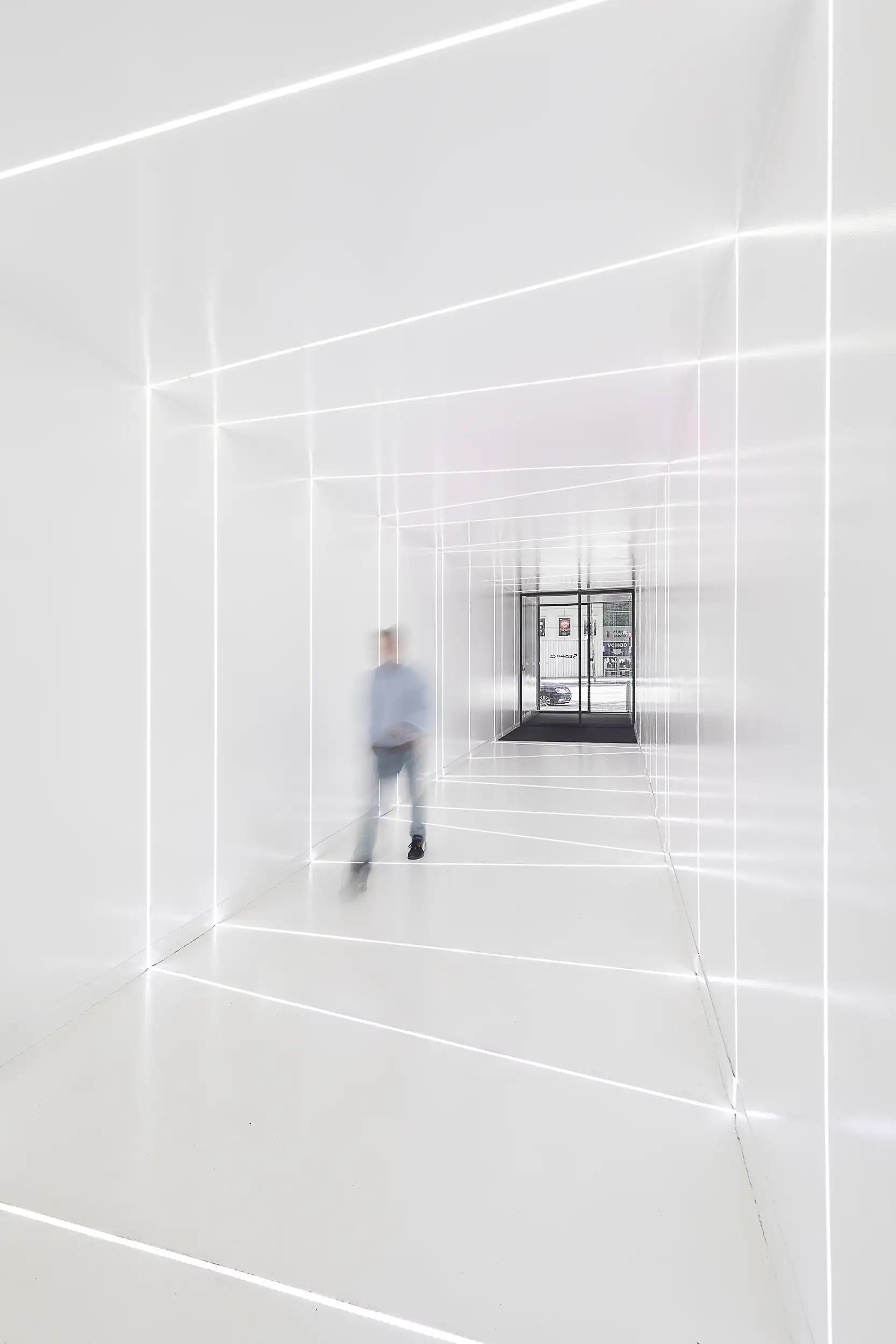 Futuristic white entrance hallway with a unique diagonal lighting design leading to Seznam.cz in Prague, Czech Republic. A blurred figure can be seen approaching through the corridor.