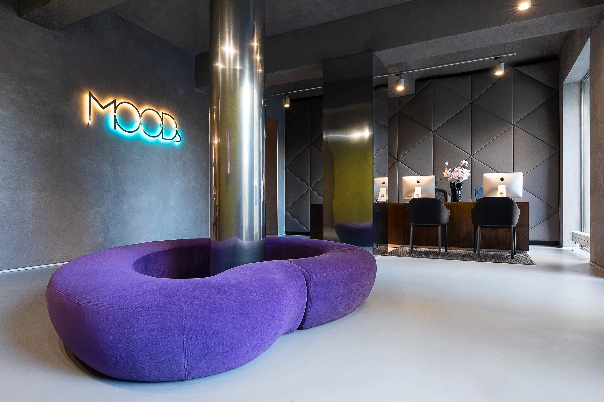 Moderne Rezeption im MOODs Boutique Hotel Prag mit violettem Rundsofa, leuchtendem Neonlogo, polygonalen Wandpaneelen und minimalistischem Design.
