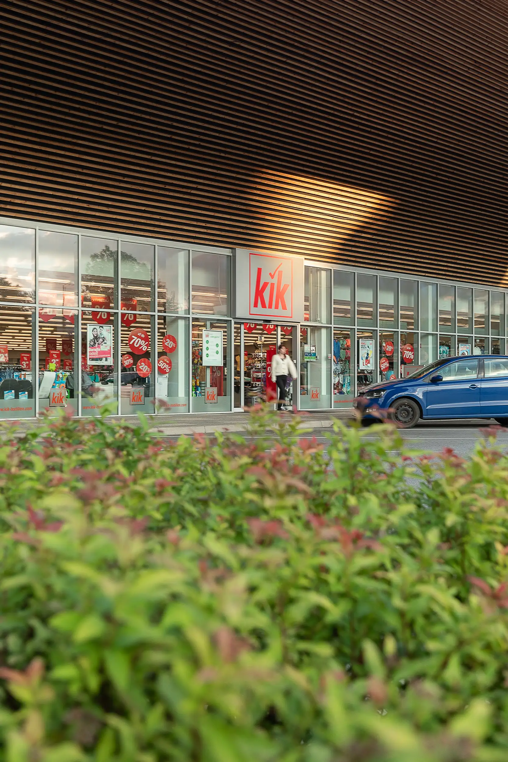 Close-up to a woman blurred in motion walking out from the KiK store in OC Solivaria in Prešov, Slovakia, captured with greenery in the lower part of the frame.