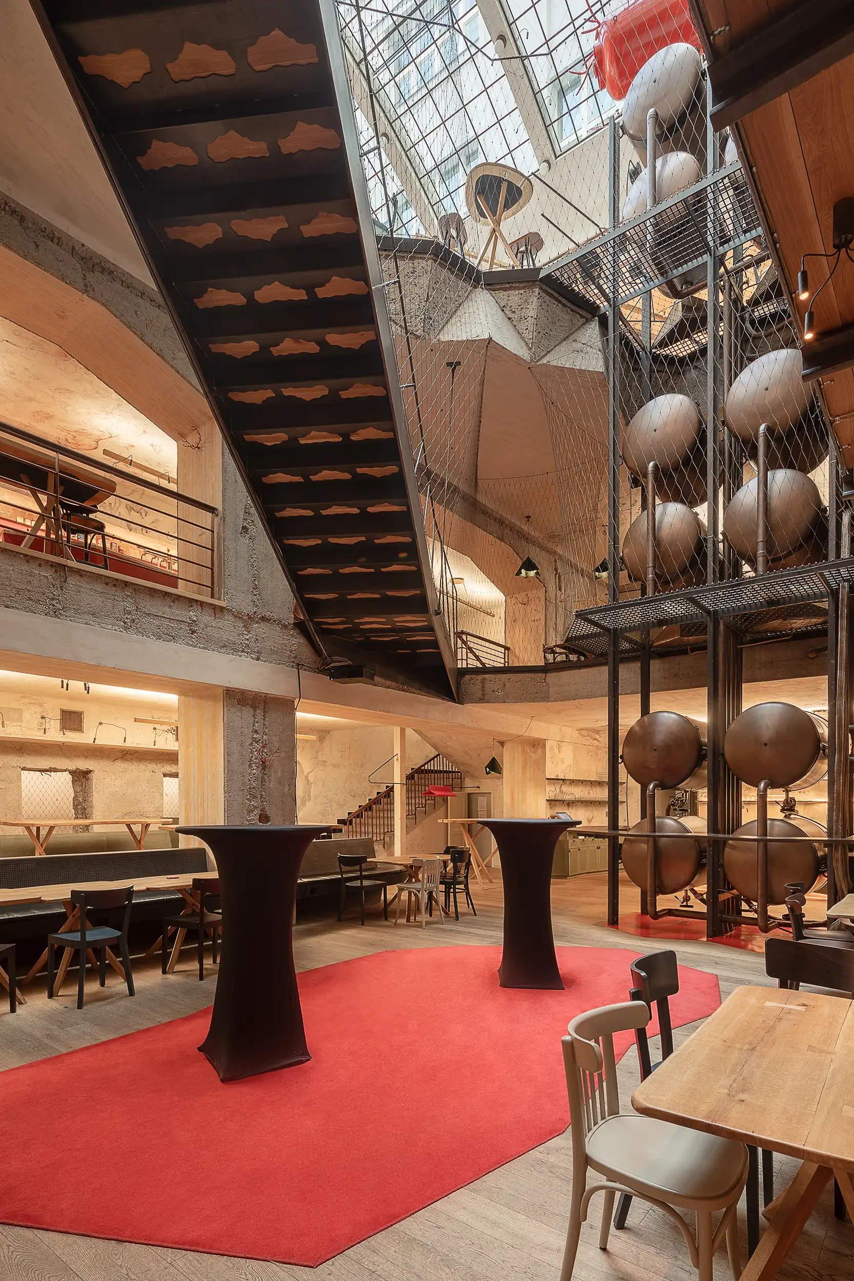 A vertical interior photograph of the underground floors of Červený Jelen restaurant located in Prague, Czech Republic, shows a cross-section view of the floors and the overall height of the space. Additionally, it showcases the tallest beer tank tower in the world.