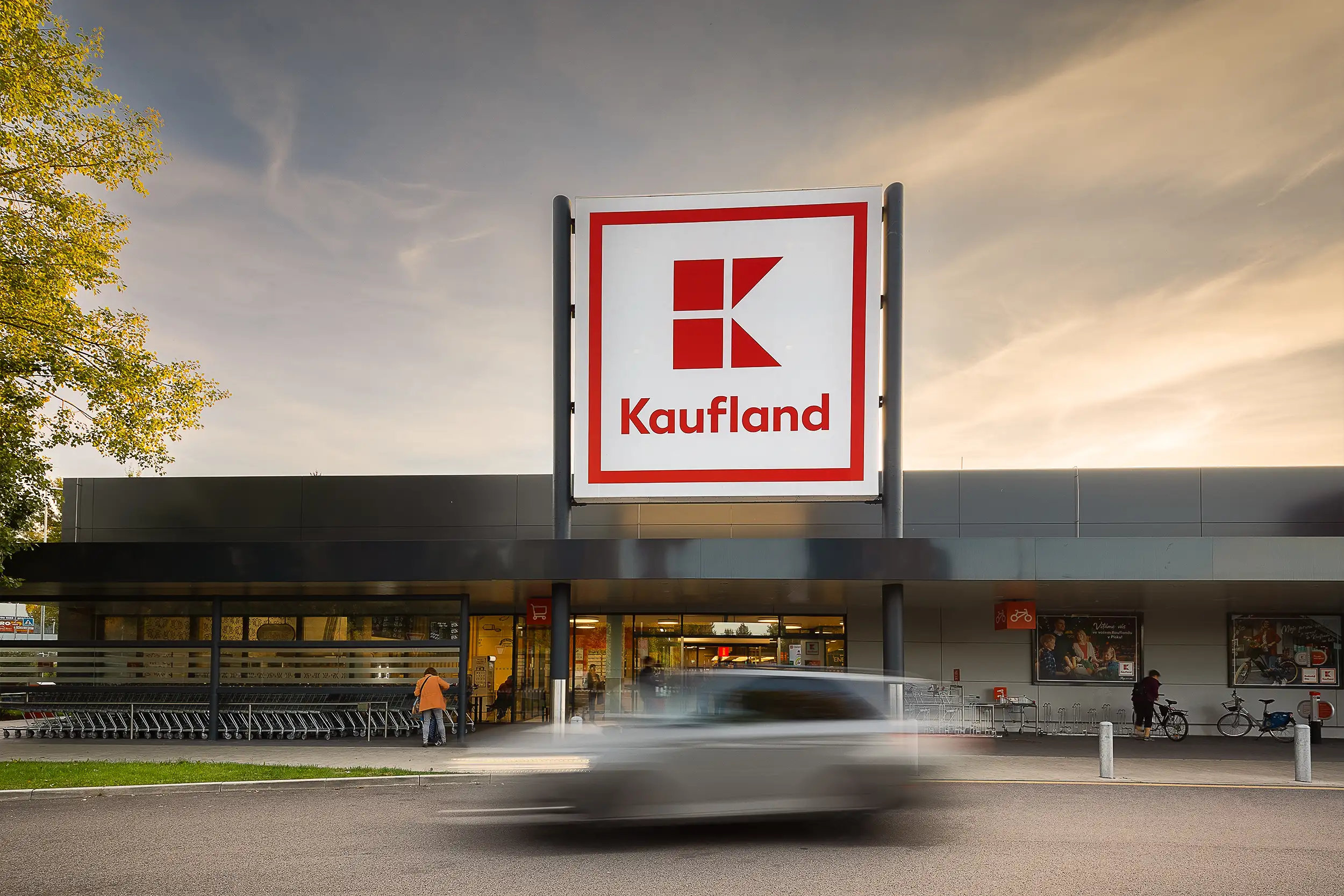 Hero image of the entrance to the newly built Kaufland store in Písek retail center captured in the golden hour, with a car, blurred in motion, passing by.