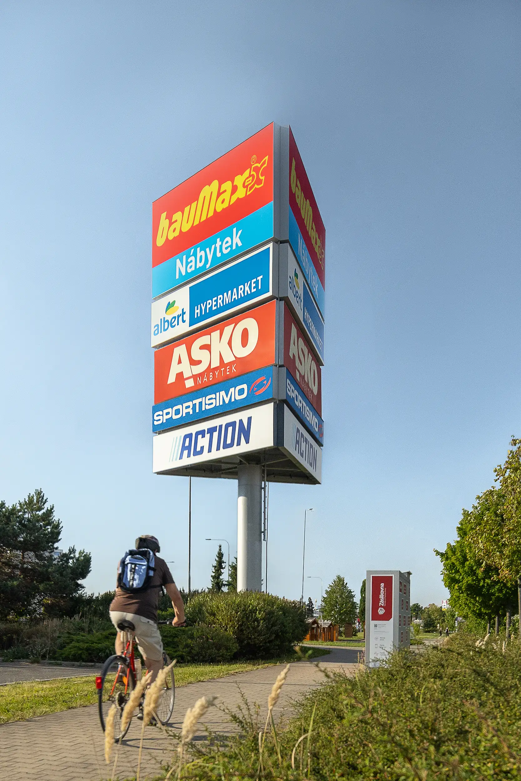 Daylight vertical photo showcasing the totem signage in front of Tabor retail center with a cyclist passing below it.