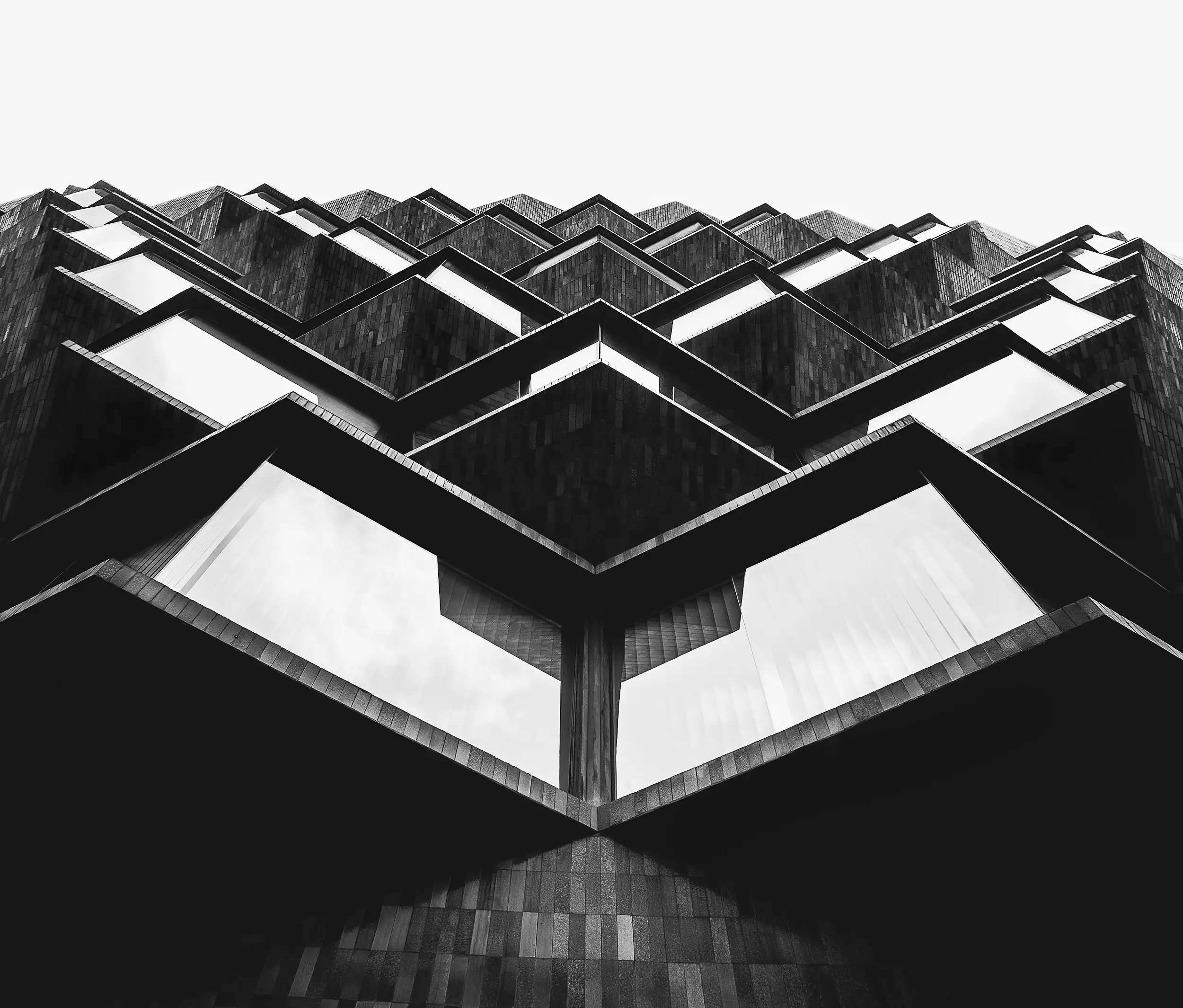 Black and white, fine art photography of architecture. A symmetrically composed upward view of the front façade of a building made up of polygons at Henao Kalea 7 in Bilbao, Spain.