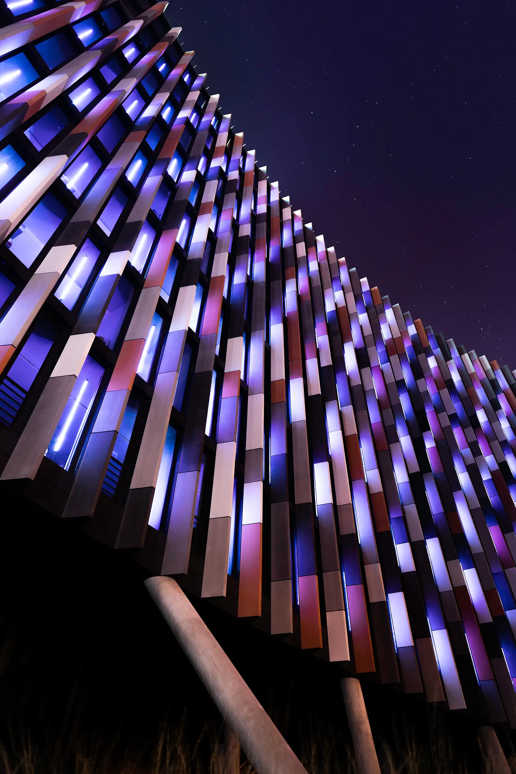 The photo captures the modern Main Point building in Prague Karlin at night from street level, showing its illuminated colored exterior wall panels.