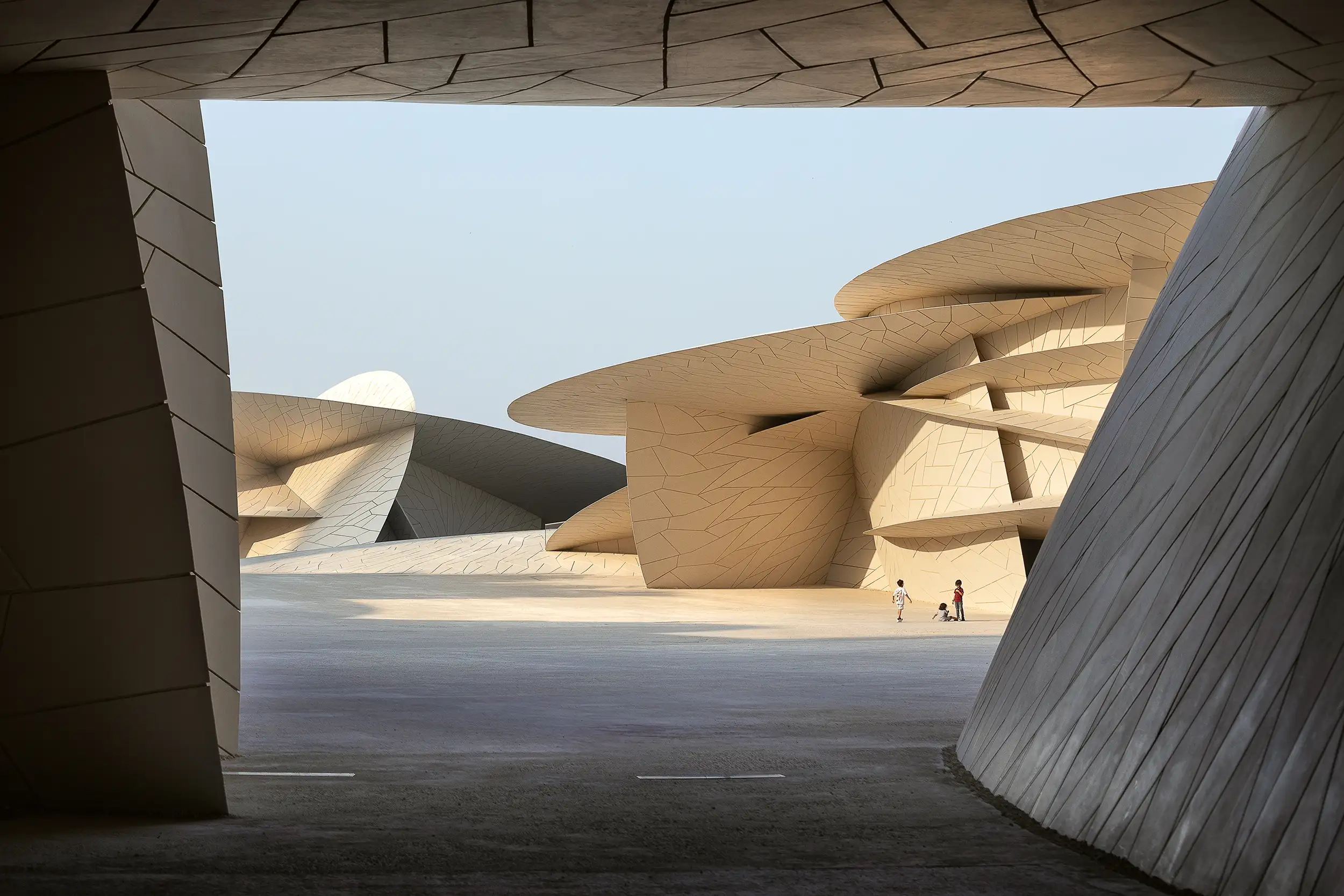 A view through the entrance to the secluded courtyard of the modern Qatar National Museum, where three children are playing.