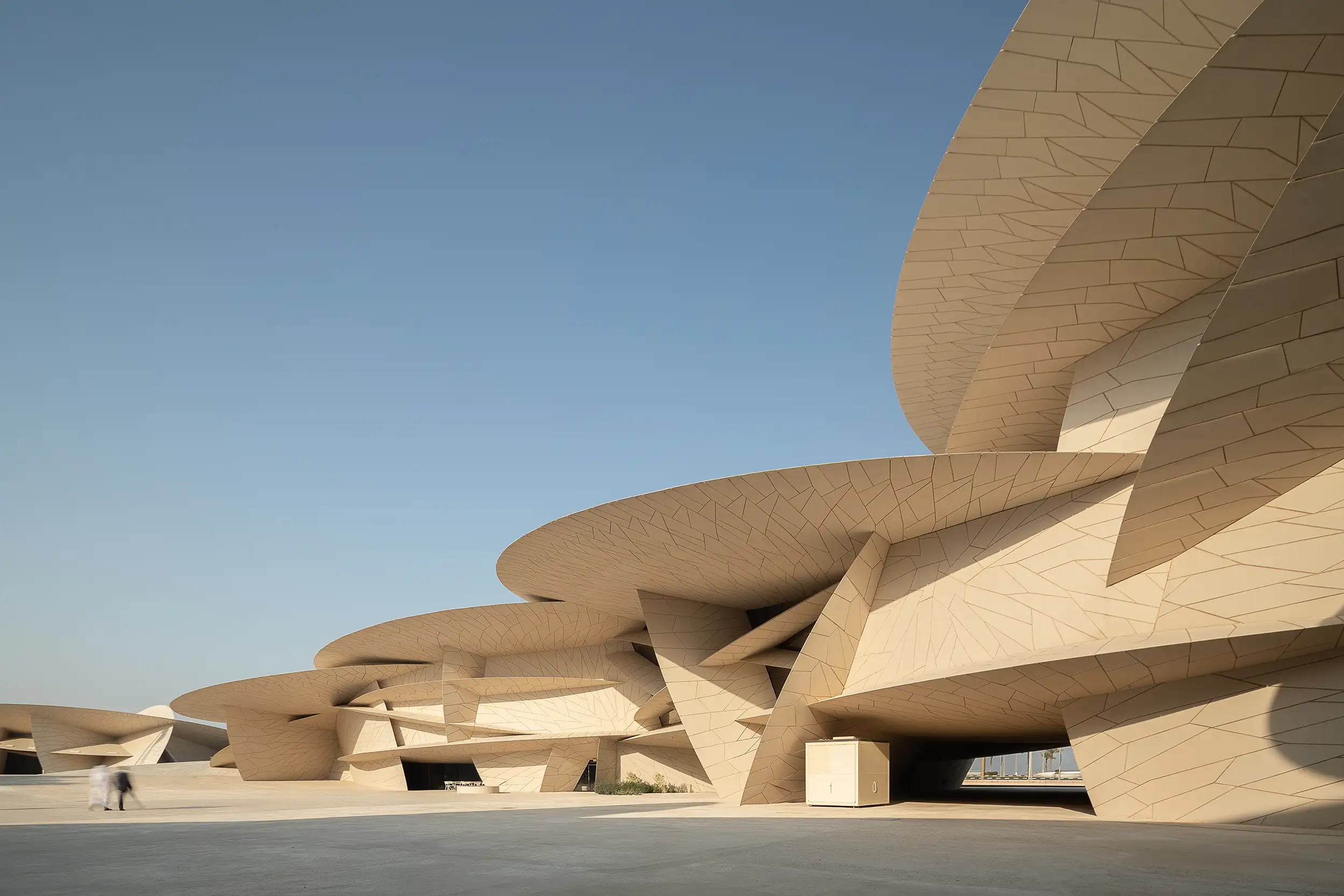 Two figures blurred in motion walk in front of the enormous modern building of the Qatar National Museum in Doha.