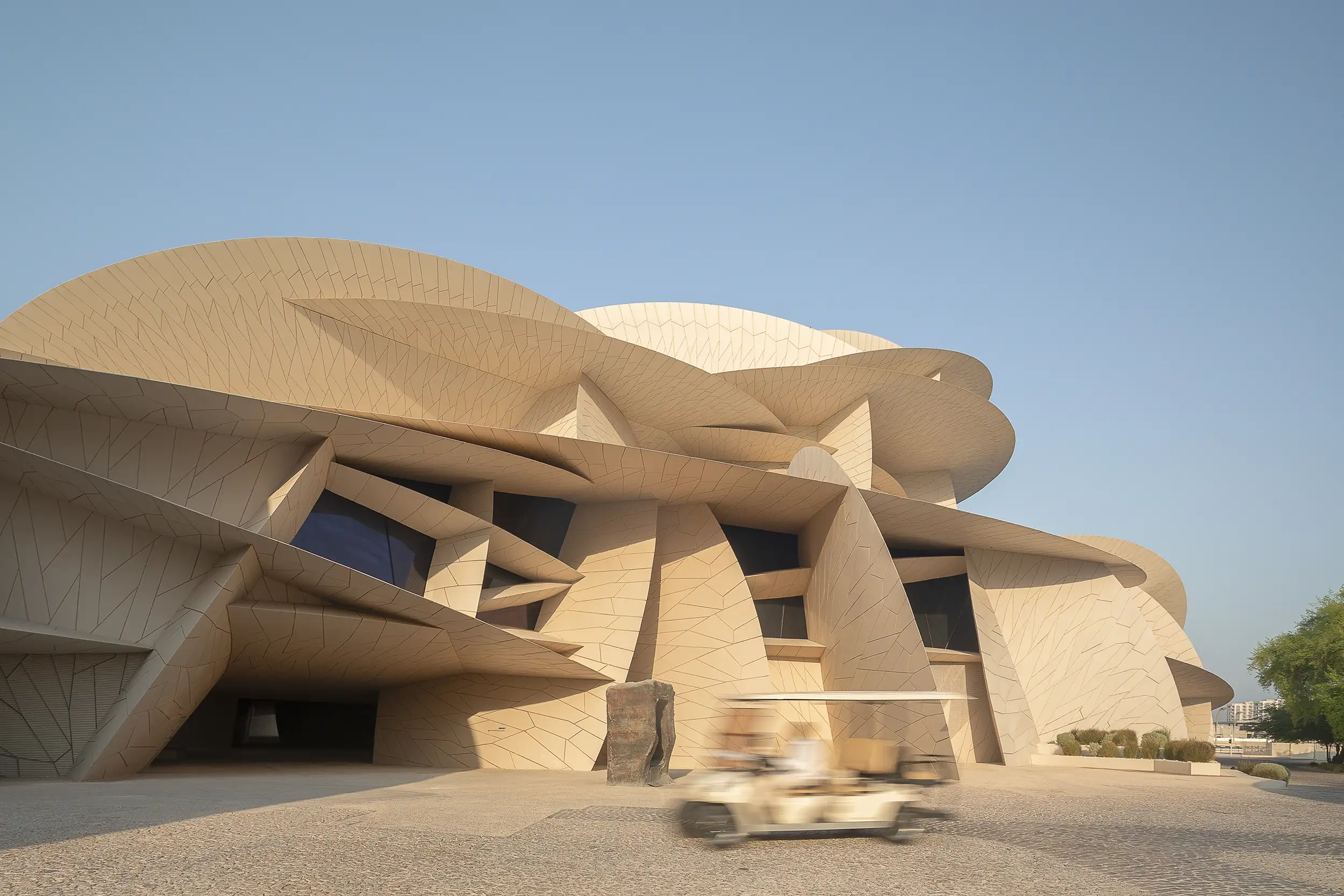 A Motion blurred transfer shuttle passing by the majestic building of National Museum of Qatar in Doha, captured from the parkside.
