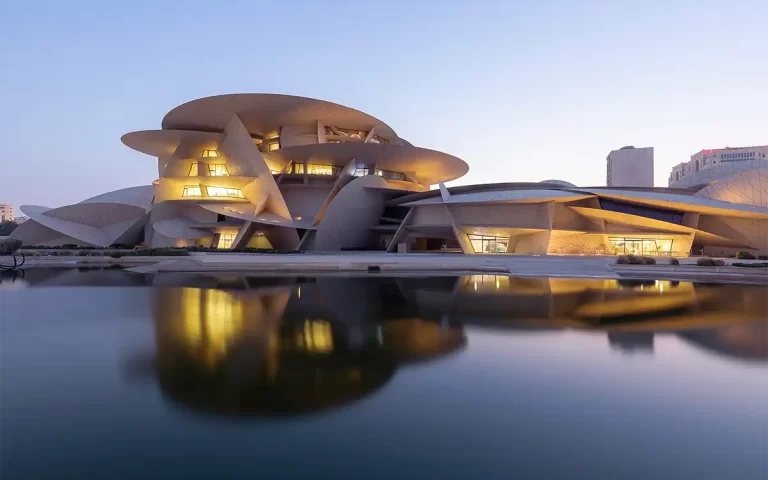 Opening photo representing architectural photography of National Museum of Qatar in Doha, view of the enlighten building with reflection in water surface.