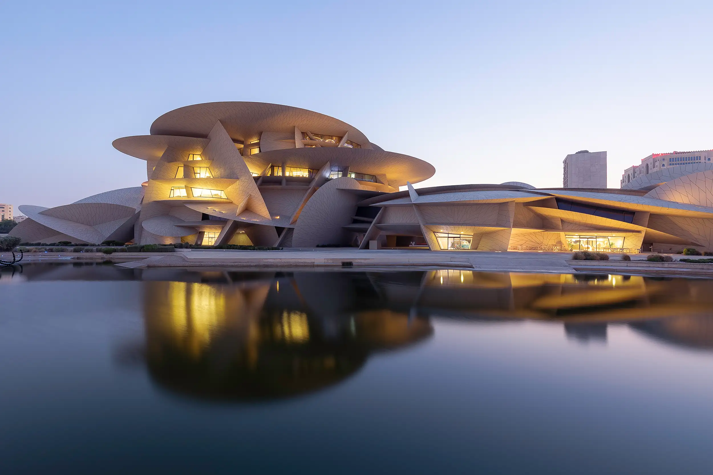 Modern National Museum of Qatar in Doha reflected in the water at dusk, photographed by architectural photographer Ondrej Hromadko.
