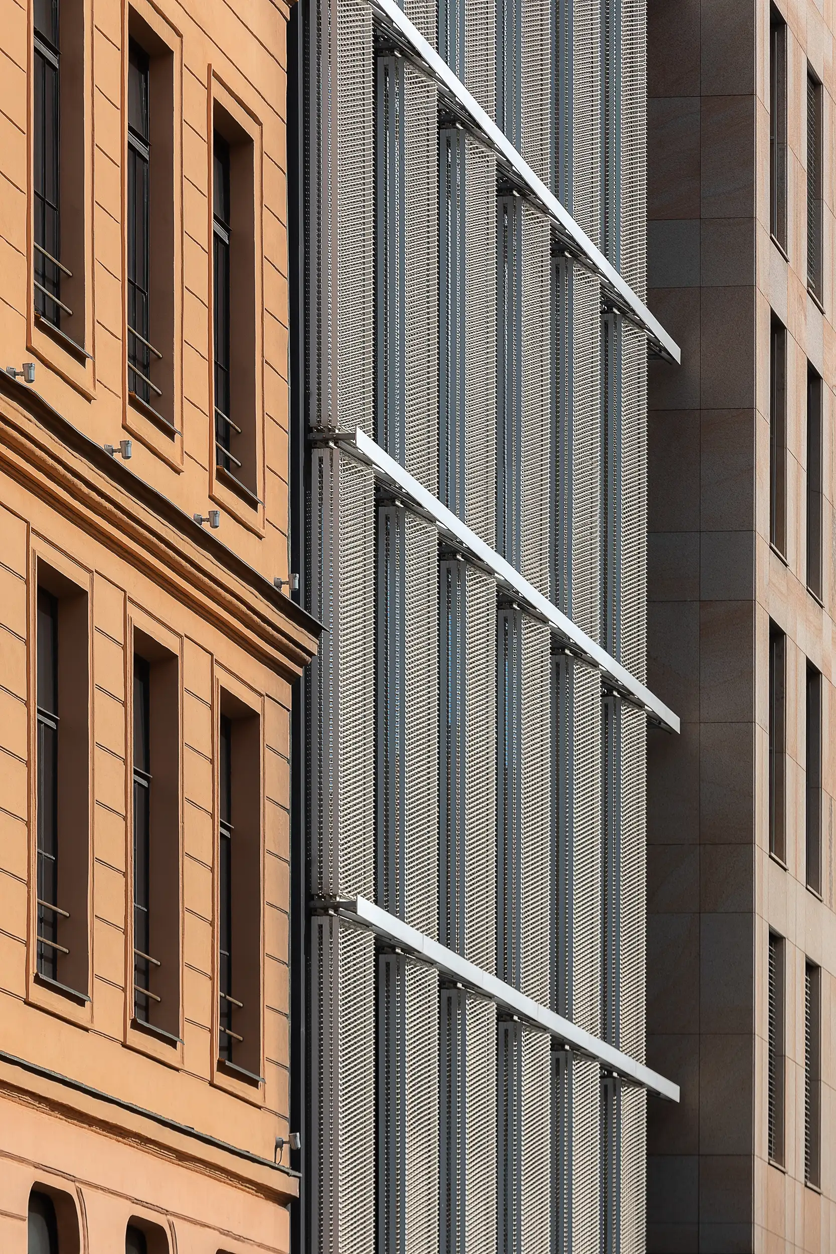 Detail photo of the three different facades of Palace Krizik in Prague, first being classicist, second covered by perforated lamellas and third being minimalistic stone cladding.
