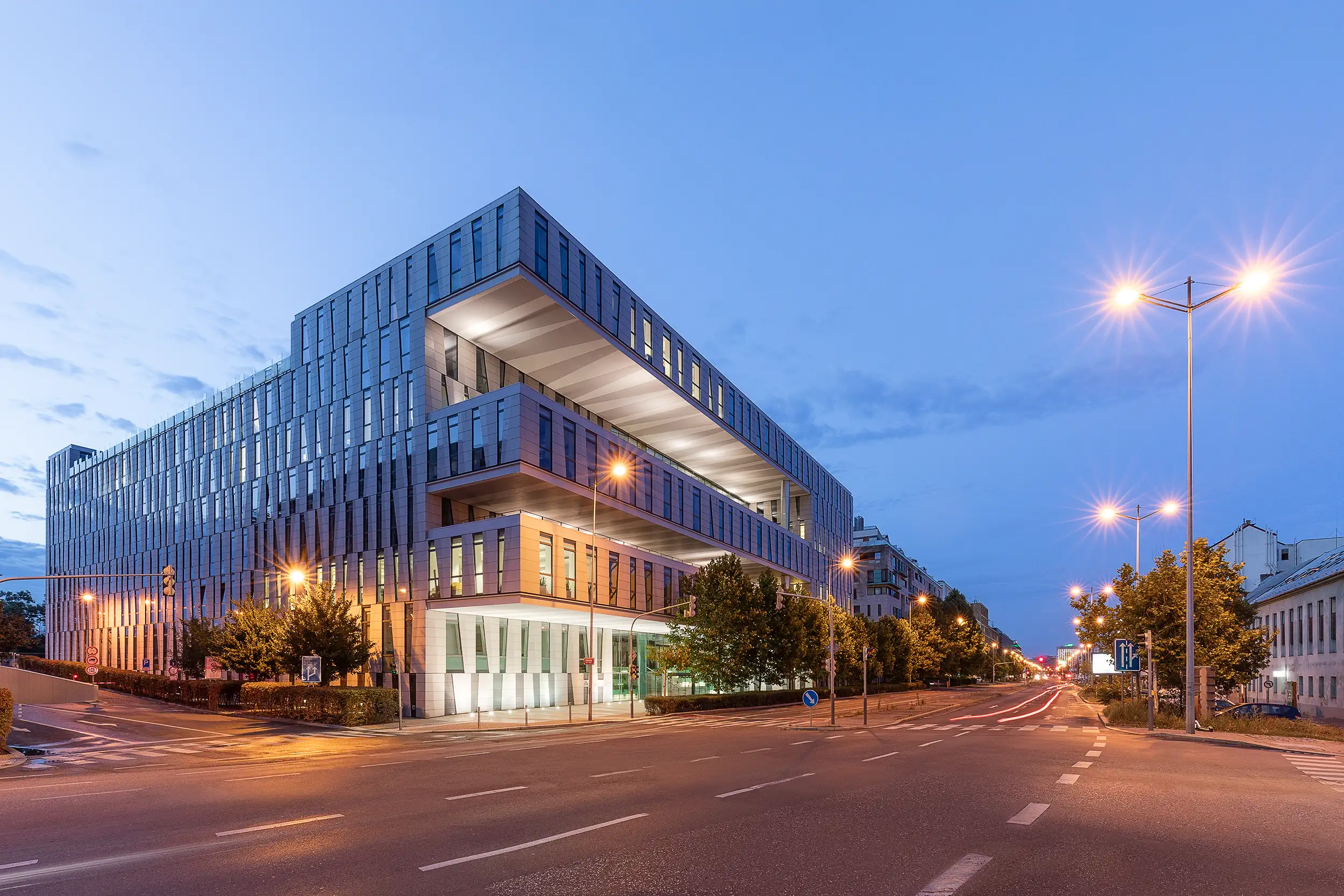 An early evening photo of the illuminated Amazon Court building in Karlín taken from a corner across the street captured by architectural photographer Ondrej Hromadko