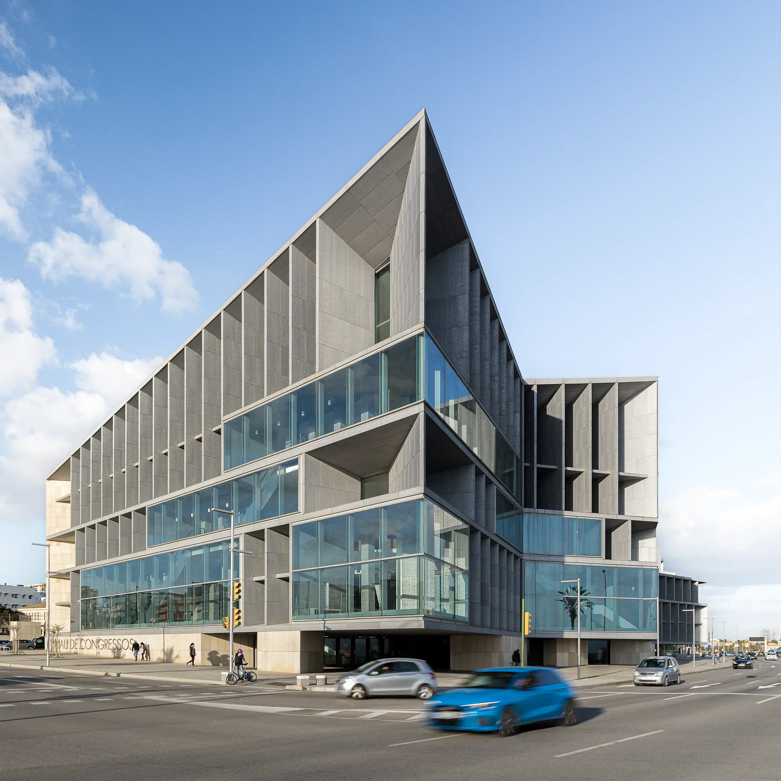 Gesamtansicht des modernen Kongresszentrums Palma mit spitzem Aufbau unregelmäßiger Geometrie, der breite Betonblöcke und vollständige Verglasung kombiniert, aufgenommen von Architekturfotograf Ondrej Hromadko.