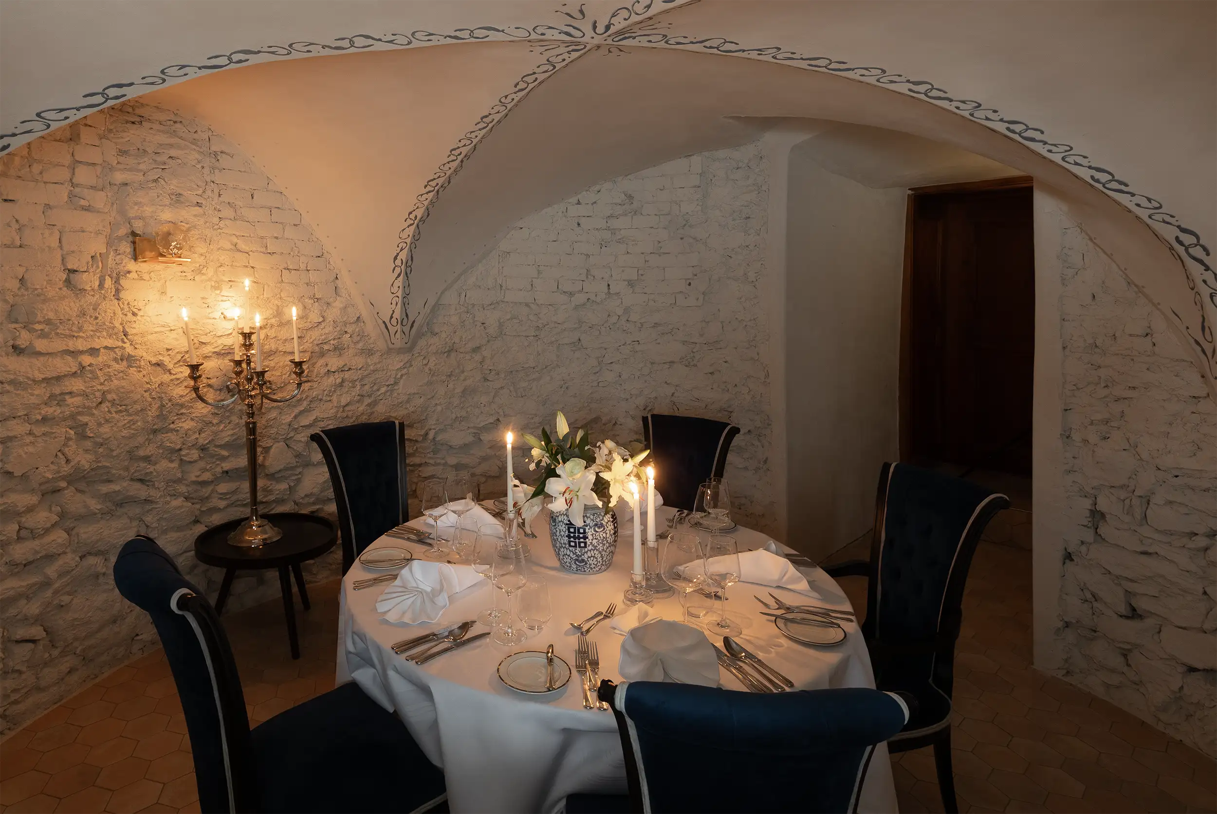 Private lounge for fine dining in castle style with stone vaulting in a moody and welcoming candlelit atmosphere.