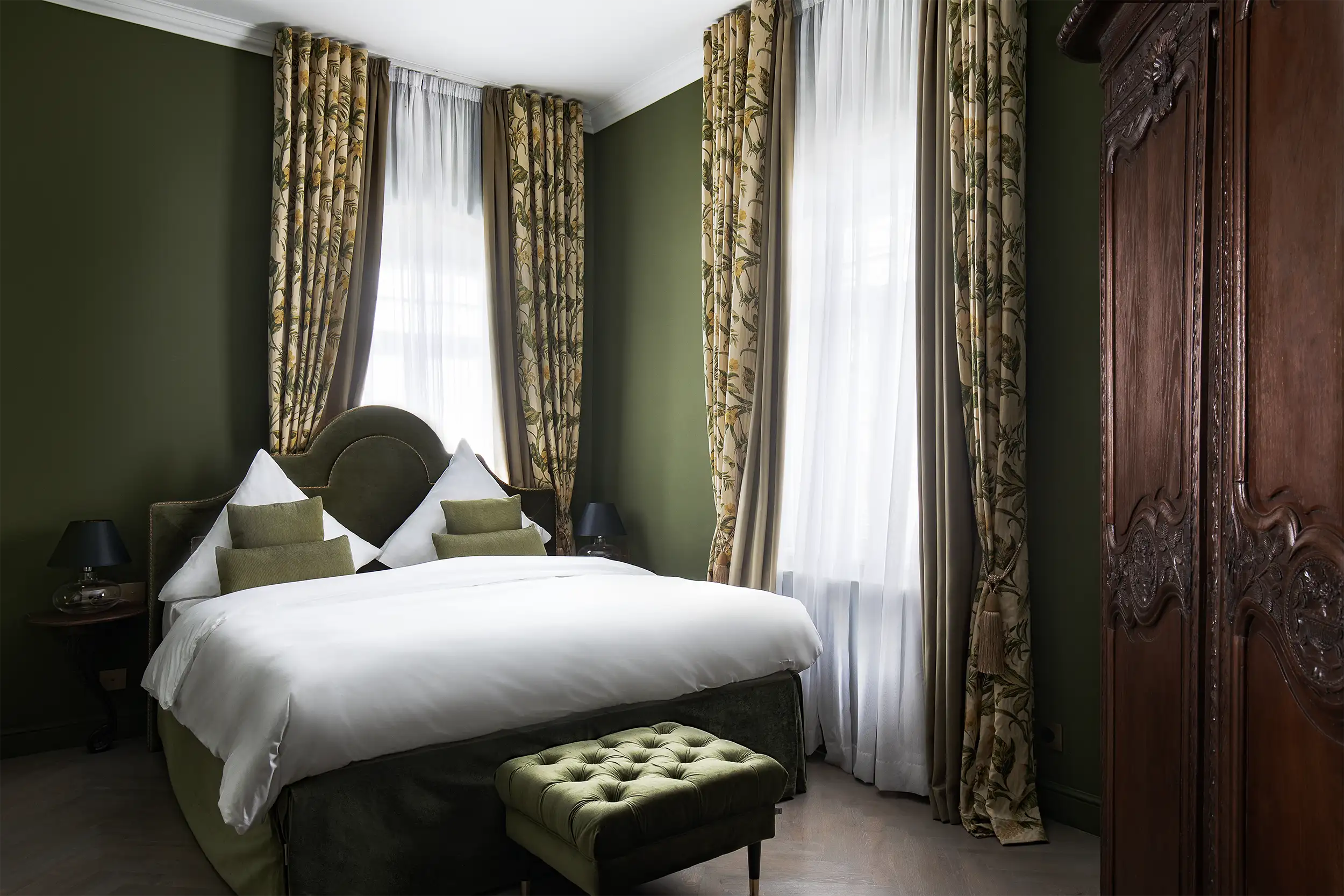 Premium old castle style hotel room with olive walls, decorative flowers curtain and wooden cabinet in foreground.