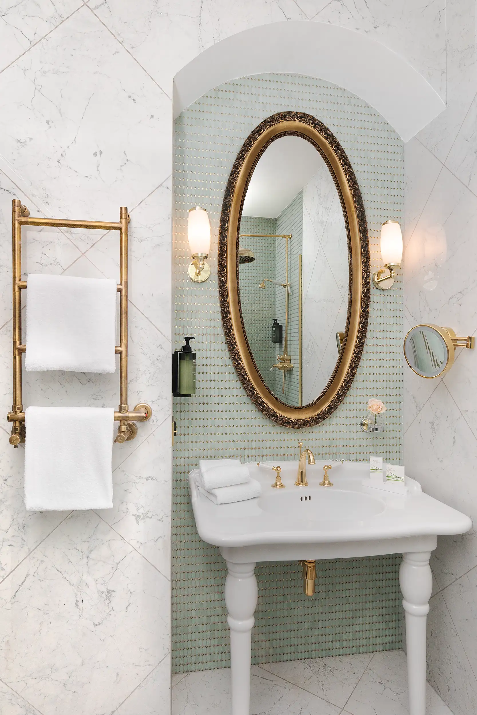 Hotel bathroom toned in pastel green colours with prominent oval mirror with old fashioned frame.