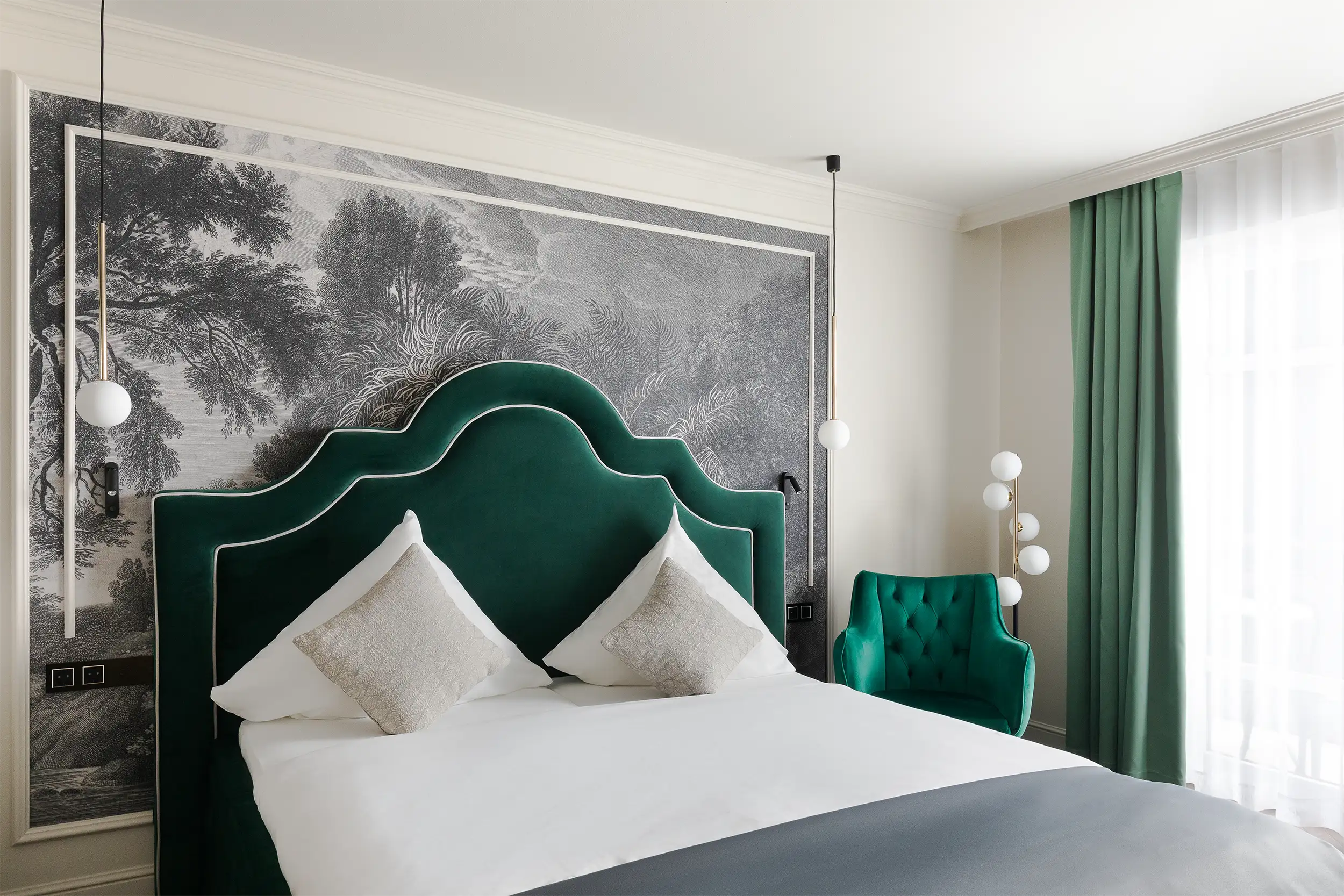 A green-coloured hotel suite with a large chateau-style bed and floral motif papering behind the bed.