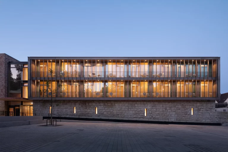 Frontal view of the modern rear extension of the Krone Oettingen Hotel with illuminated rooms at dusk.