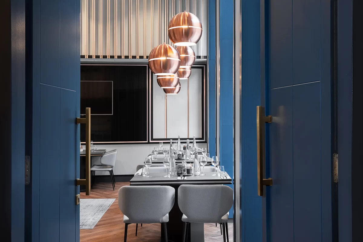 Blick durch eine angelehnte Tür in das Restaurant des Radisson Blu Prague mit gedeckten Tischen und eleganten Details in Blau- und Bronzetönen.