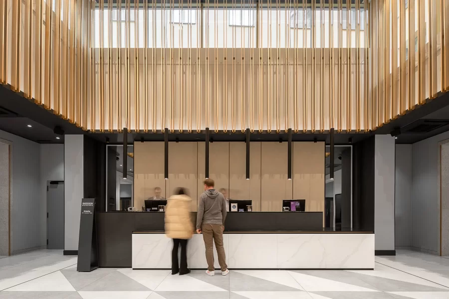 Čelně zachycená minimalistická recepce hotelu Radisson Blu v Praze, s vysokými stropy, zlatými nástěnnými dekoracemi a pohybově rozostřenými hosty v popředí.