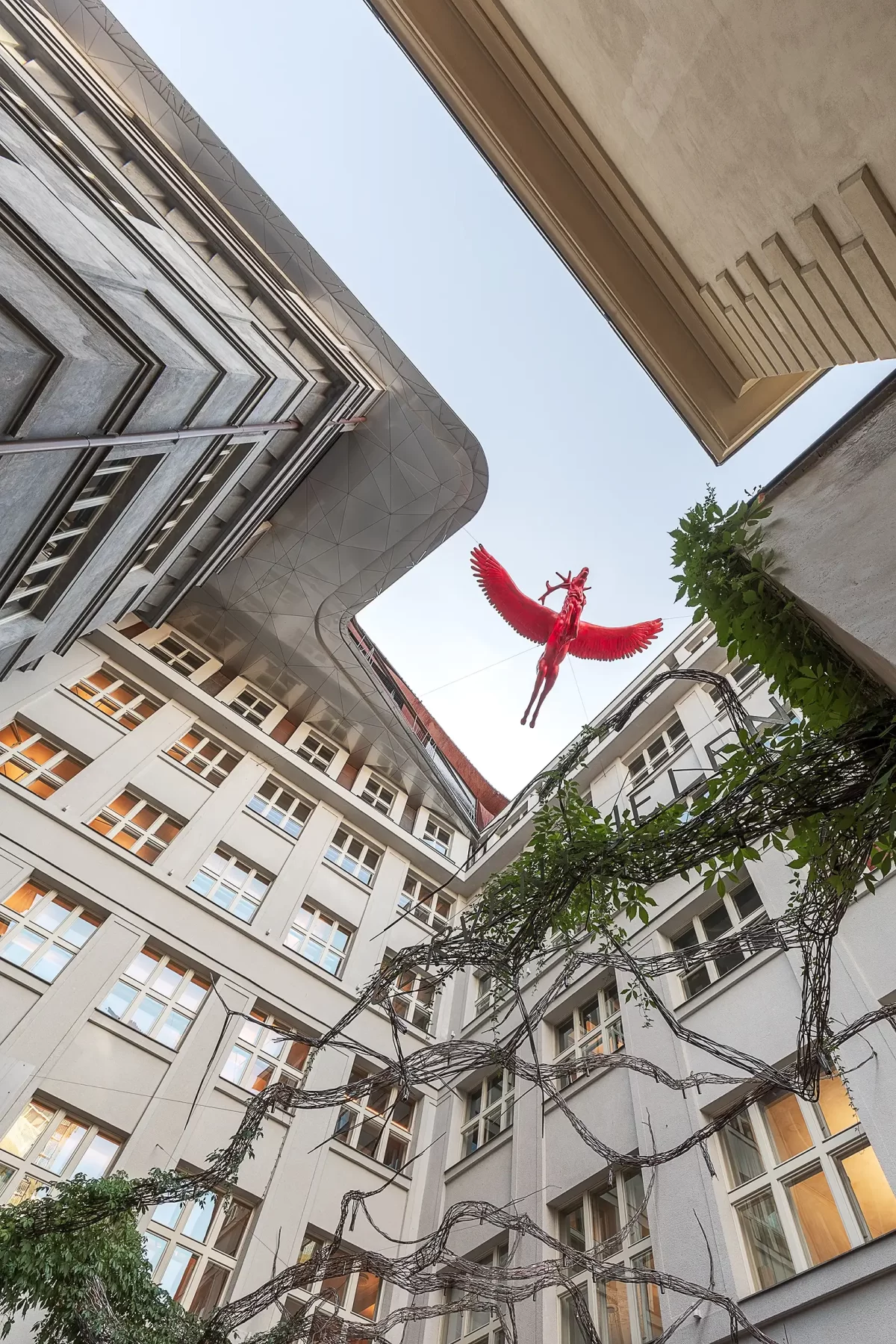 A view from the courtyard of the Špork Palace in Prague looks up at a flying red stag sculpture hanging in the center of the composition.