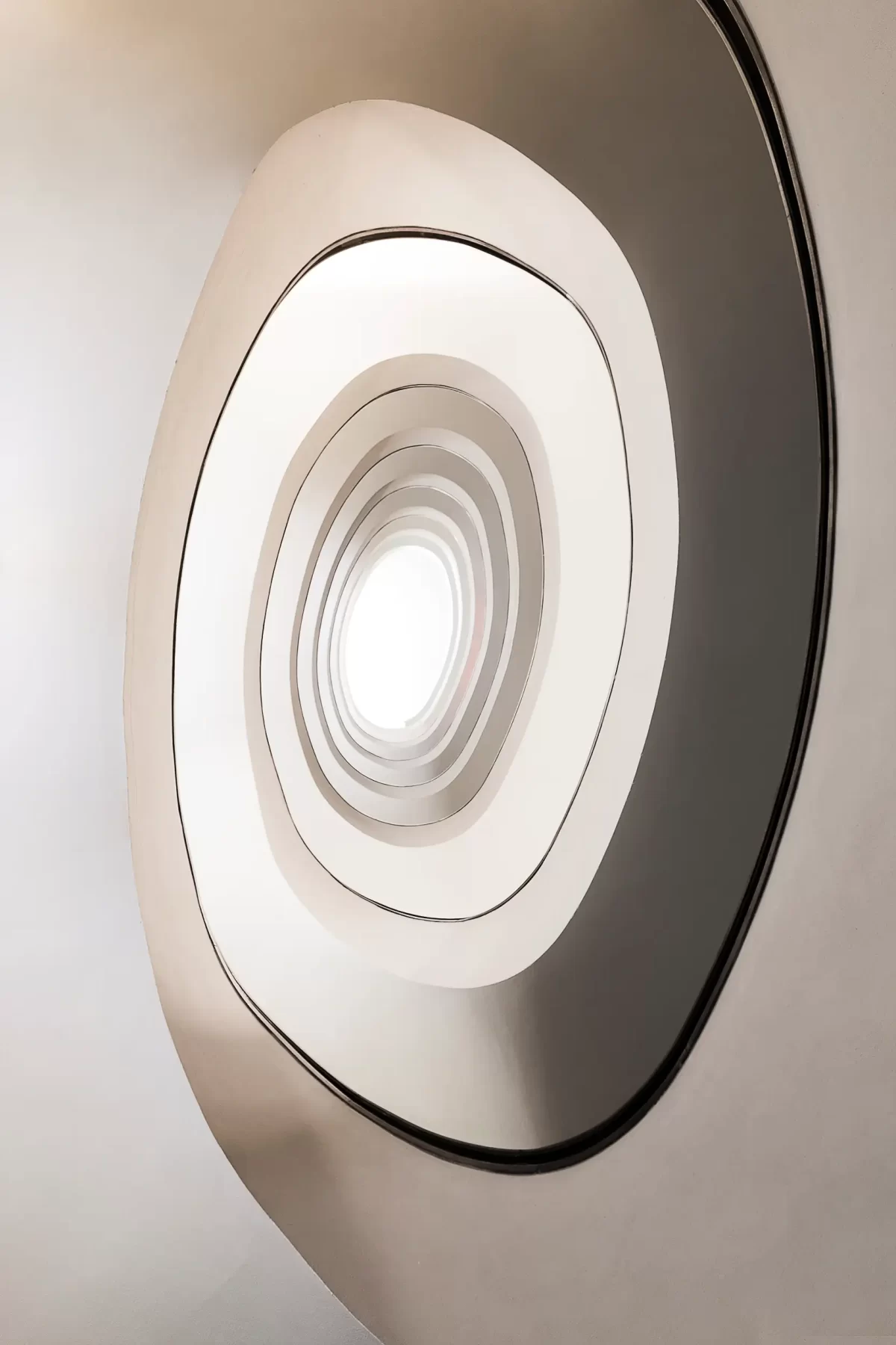 Umělecká fotografie architektury vyobrazuje téměř nekonečný pohled vzhůru na bílé minimalistické spirálové schodiště v Portu.