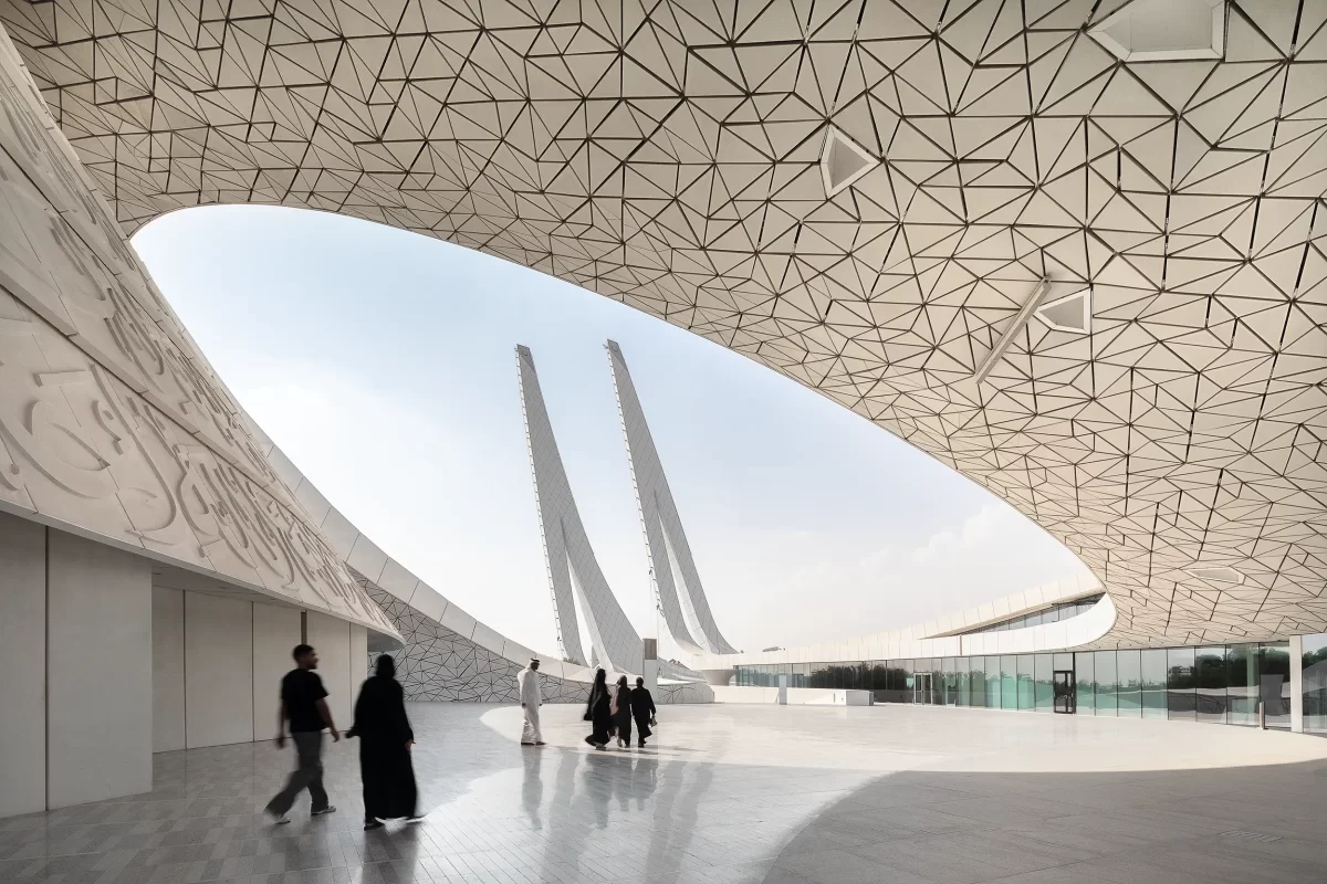 View of the modern minaret towers framed by the oval roof of the HBKU Minaretein building in Education City, Doha(Qatar), reflected in the marble floor. A group of worshippers, blurred by movement, are just exiting the mosque.