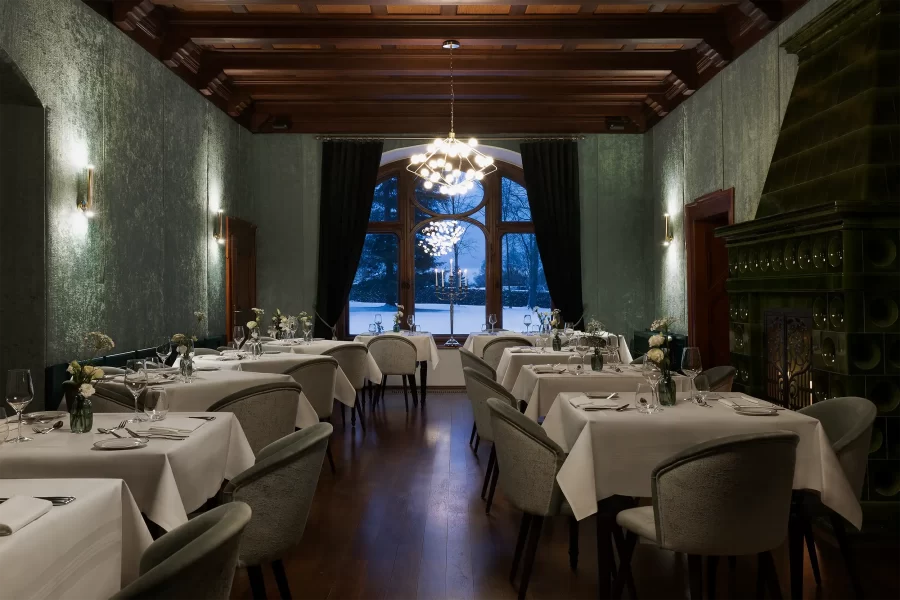 Schwach beleuchtetes Restaurant im Schlosshotel Althörnitz mit großem Fenster und Blick auf die verschneite Parklandschaft.