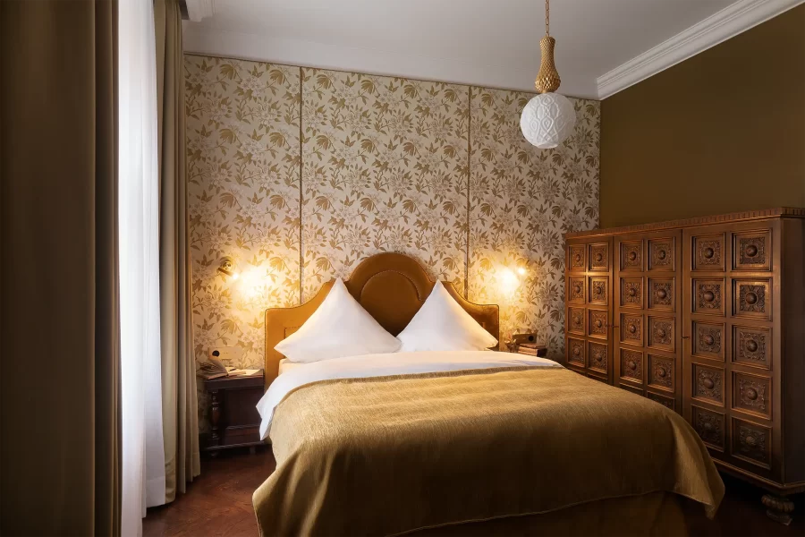 Luxuriöses Hotelzimmer im Schlossstil, in Beige-Gold-Tönen gehalten, mit einer massiven Kommode aus Holz.